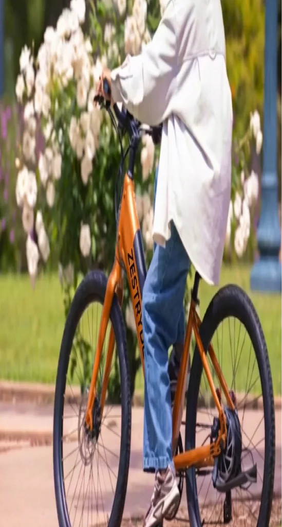 A rider passing flowering bushes on an orange ZestRyde bike